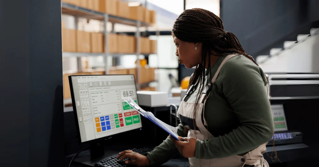 Mulher verificando dados em um sistema de computador para controle de estoque em depósito, garantindo eficiência operacional.