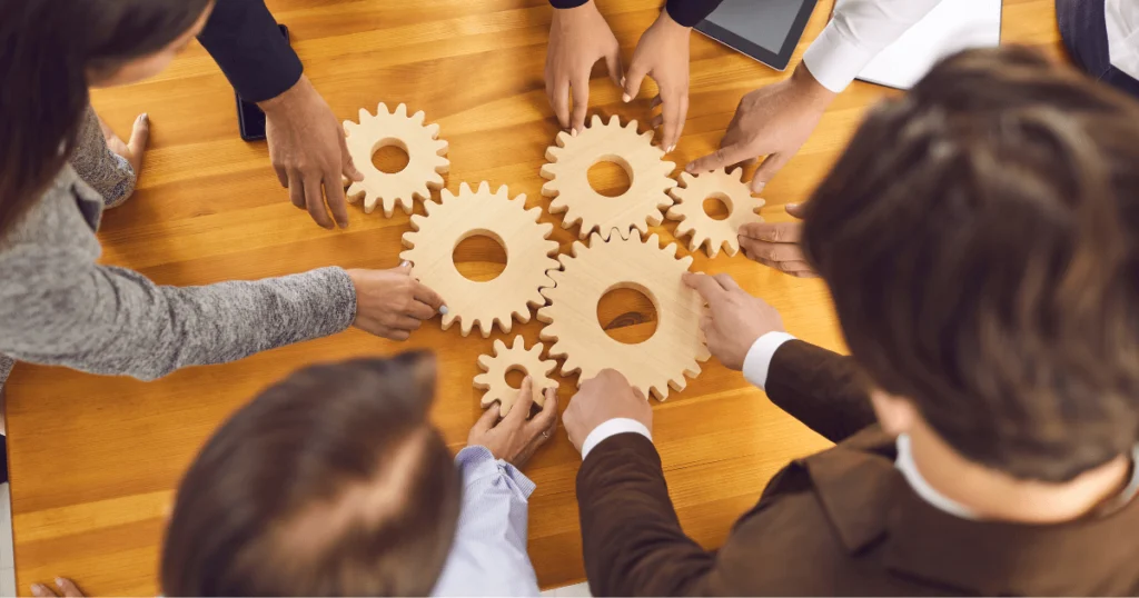 Mãos unidas movimentando engrenagens de madeira, simbolizando colaboração e integração completa para melhorar processos empresariais.